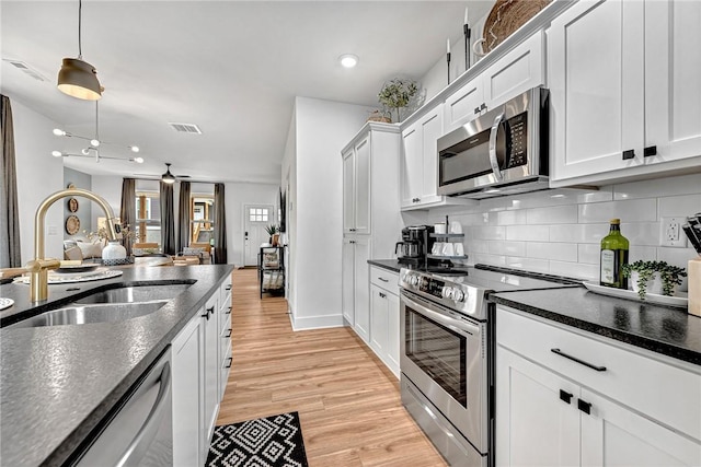 kitchen featuring decorative light fixtures, sink, white cabinets, stainless steel appliances, and light wood-type flooring