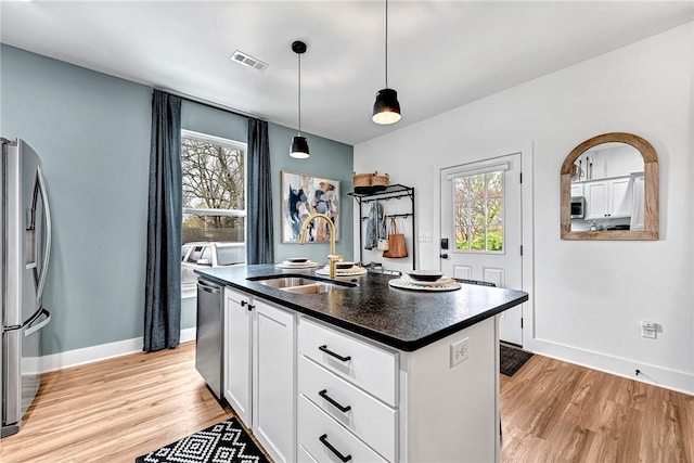 kitchen featuring sink, appliances with stainless steel finishes, a kitchen island with sink, hanging light fixtures, and white cabinets