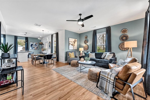 living room featuring ceiling fan with notable chandelier and light hardwood / wood-style floors