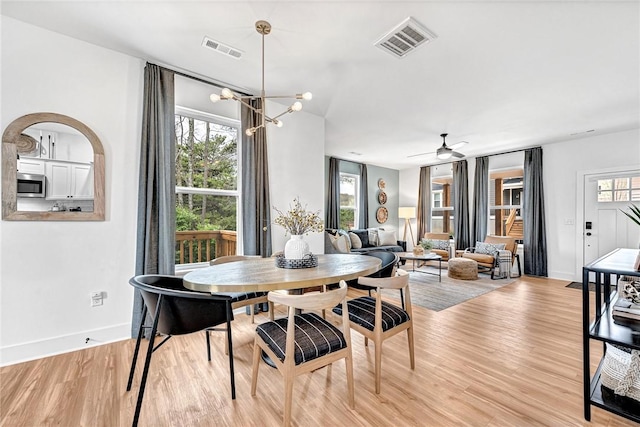 dining space featuring ceiling fan with notable chandelier, a wealth of natural light, and light hardwood / wood-style flooring