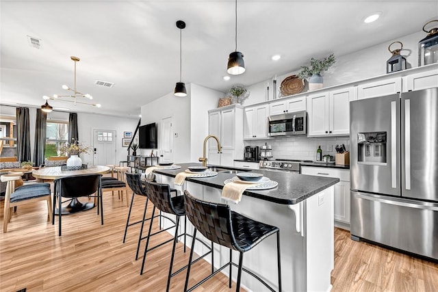 kitchen with appliances with stainless steel finishes, a breakfast bar, an island with sink, white cabinets, and hanging light fixtures