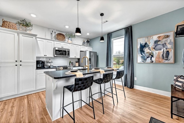 kitchen featuring stainless steel appliances, white cabinetry, a kitchen island with sink, and decorative light fixtures