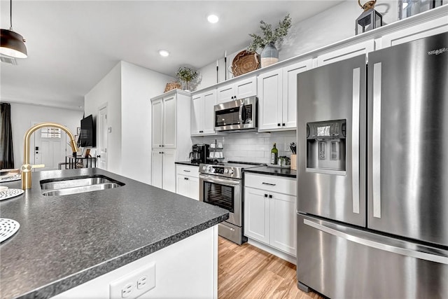 kitchen with sink, white cabinetry, backsplash, stainless steel appliances, and light hardwood / wood-style floors