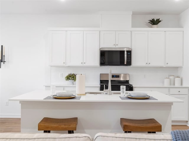 kitchen with white cabinetry, a kitchen bar, a kitchen island with sink, and appliances with stainless steel finishes