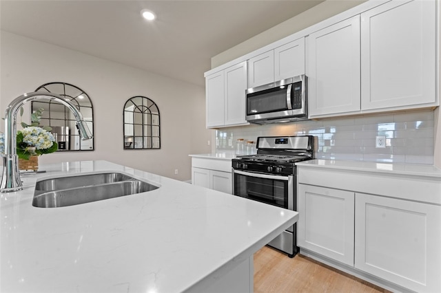 kitchen featuring light wood-type flooring, light stone counters, sink, white cabinetry, and appliances with stainless steel finishes