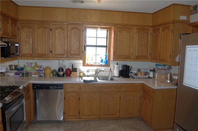 kitchen with light tile patterned flooring, sink, tasteful backsplash, a textured ceiling, and appliances with stainless steel finishes