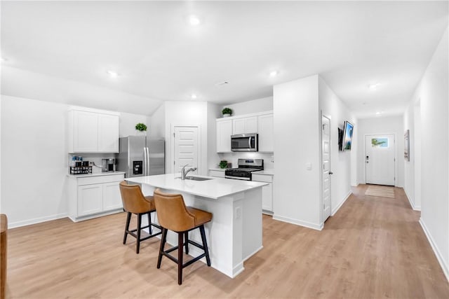 kitchen with a sink, stainless steel appliances, a breakfast bar area, white cabinets, and light countertops