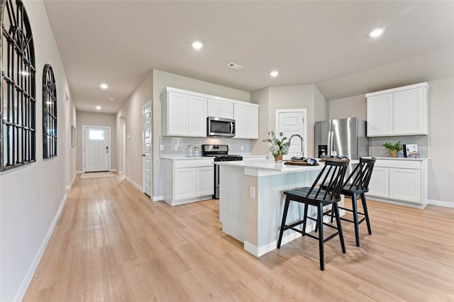 kitchen with white cabinets, a kitchen island with sink, stainless steel appliances, a breakfast bar, and light hardwood / wood-style floors