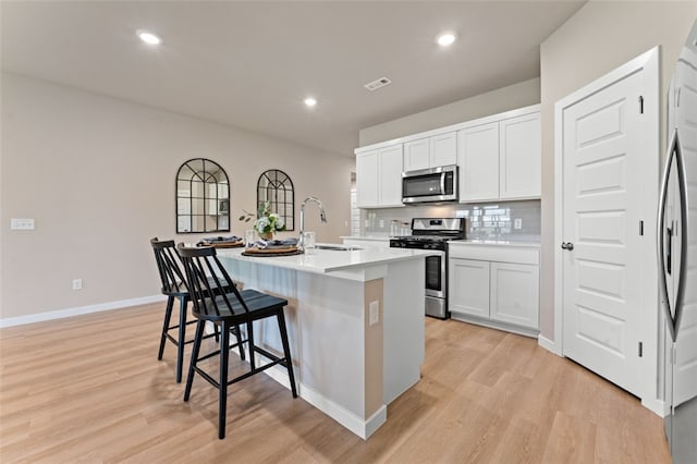 kitchen with light hardwood / wood-style flooring, a kitchen island with sink, appliances with stainless steel finishes, and white cabinetry