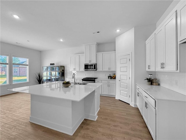 kitchen featuring sink, a center island with sink, white cabinetry, stainless steel appliances, and light wood-type flooring