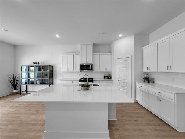 kitchen with a center island with sink, light hardwood / wood-style floors, white cabinetry, and light stone counters