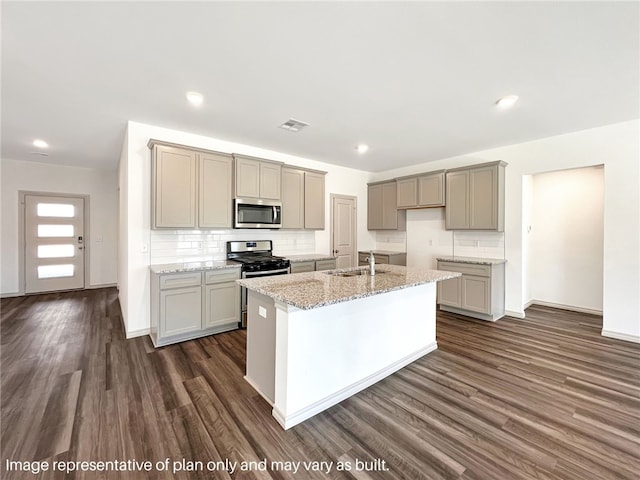 kitchen with a kitchen island with sink, sink, dark hardwood / wood-style flooring, light stone counters, and stainless steel appliances