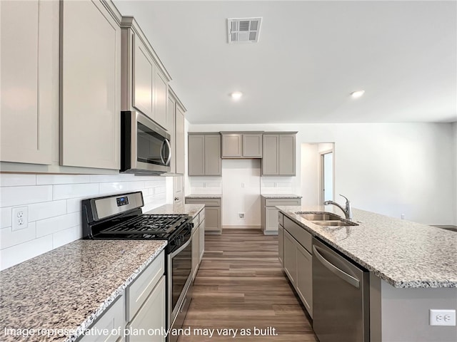 kitchen featuring sink, light stone counters, dark hardwood / wood-style floors, a kitchen island with sink, and appliances with stainless steel finishes