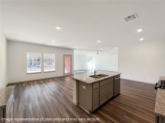 kitchen featuring light stone countertops, dark wood-type flooring, sink, dishwasher, and an island with sink