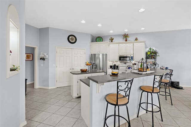 kitchen with appliances with stainless steel finishes, light tile patterned flooring, an island with sink, a breakfast bar, and white cabinets