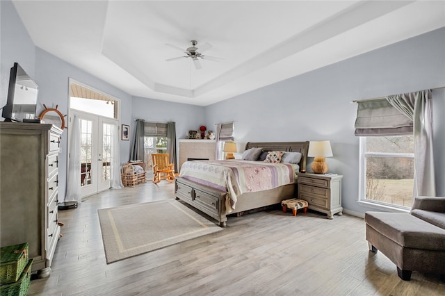 bedroom featuring a raised ceiling, light hardwood / wood-style floors, ceiling fan, and french doors