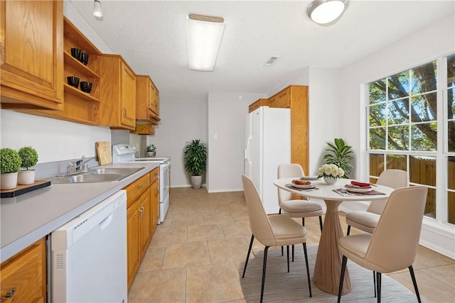 kitchen with a textured ceiling, white appliances, sink, and light tile patterned floors