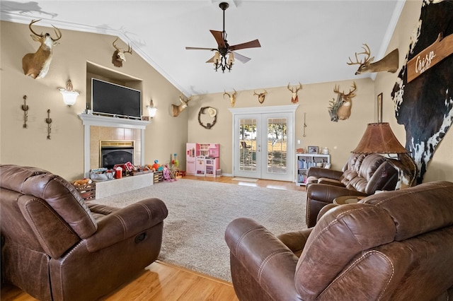 living room featuring french doors, light hardwood / wood-style flooring, a tile fireplace, crown molding, and vaulted ceiling