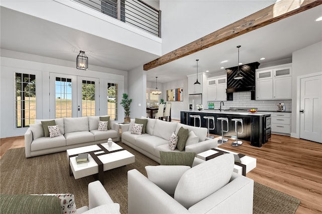 living room with a high ceiling, light hardwood / wood-style floors, beamed ceiling, and sink