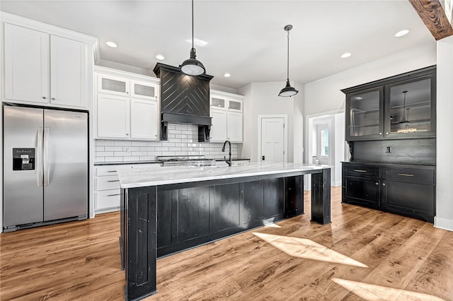 kitchen featuring an island with sink, light hardwood / wood-style flooring, backsplash, decorative light fixtures, and stainless steel fridge