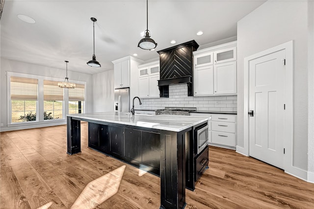 kitchen featuring hanging light fixtures, a center island with sink, white cabinetry, stainless steel appliances, and light hardwood / wood-style floors