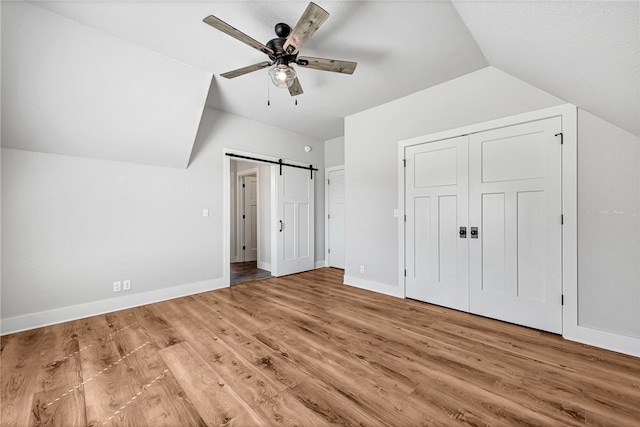 unfurnished bedroom featuring a barn door, lofted ceiling, ceiling fan, and hardwood / wood-style flooring