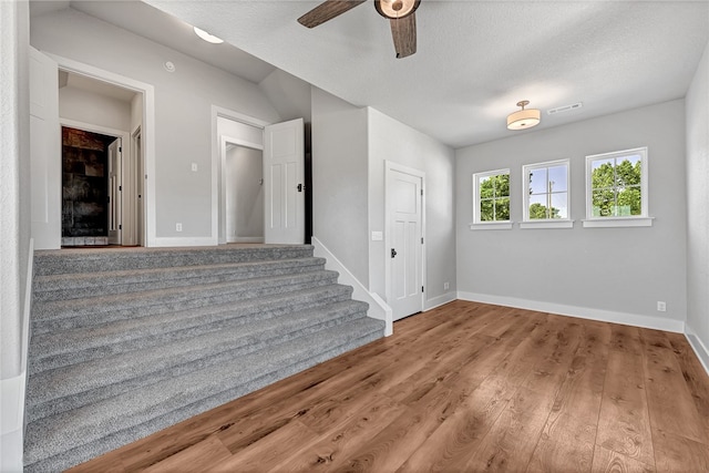 stairway with a textured ceiling, hardwood / wood-style floors, and ceiling fan