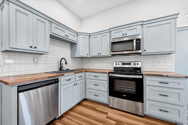 kitchen with sink, backsplash, appliances with stainless steel finishes, light hardwood / wood-style floors, and wood counters