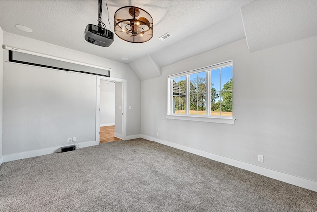 unfurnished bedroom with a textured ceiling, lofted ceiling, and carpet floors