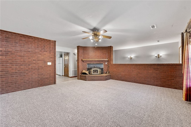 unfurnished living room with ceiling fan, a wood stove, light carpet, and brick wall