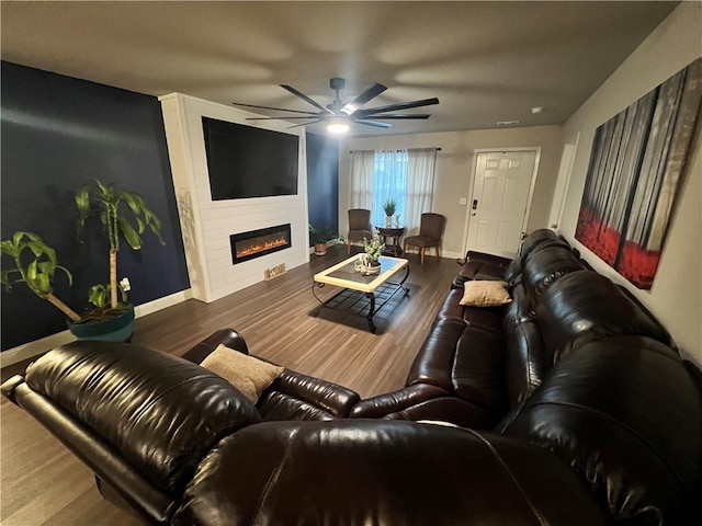 living room with ceiling fan, dark wood-type flooring, and a large fireplace