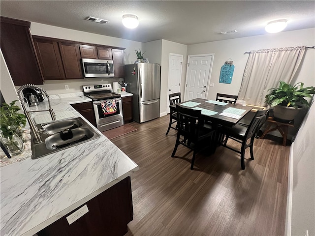 kitchen with dark wood-type flooring, stainless steel appliances, a textured ceiling, dark brown cabinetry, and sink