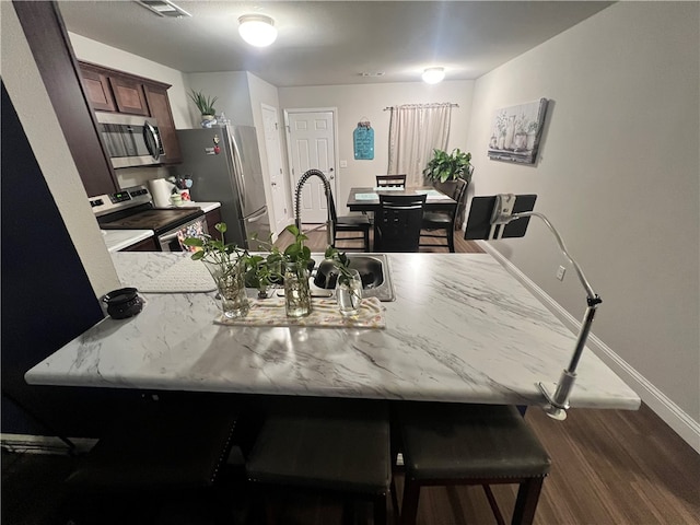 kitchen featuring sink, kitchen peninsula, stainless steel appliances, a kitchen bar, and dark hardwood / wood-style flooring