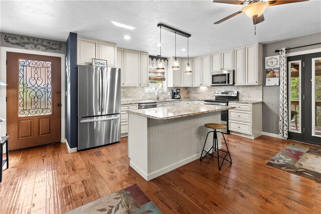 kitchen with light stone countertops, appliances with stainless steel finishes, light hardwood / wood-style flooring, and a kitchen island