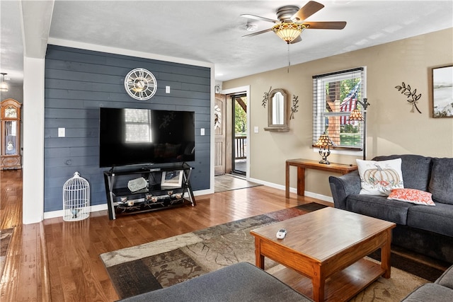 living room with ceiling fan, a wealth of natural light, wooden walls, and hardwood / wood-style floors