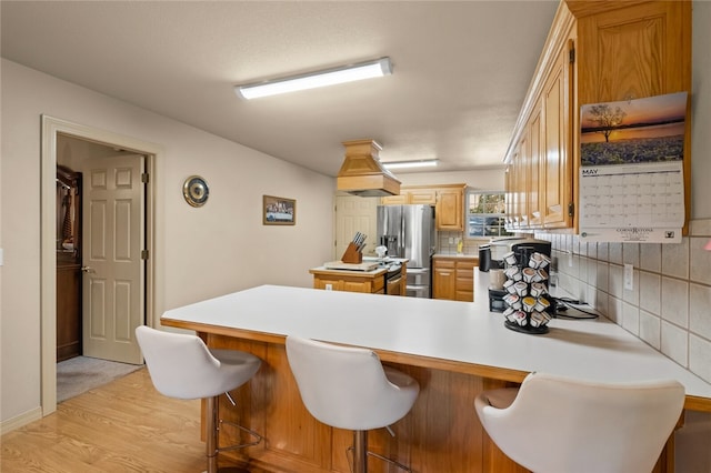 kitchen featuring a breakfast bar, backsplash, light hardwood / wood-style flooring, stainless steel fridge, and kitchen peninsula