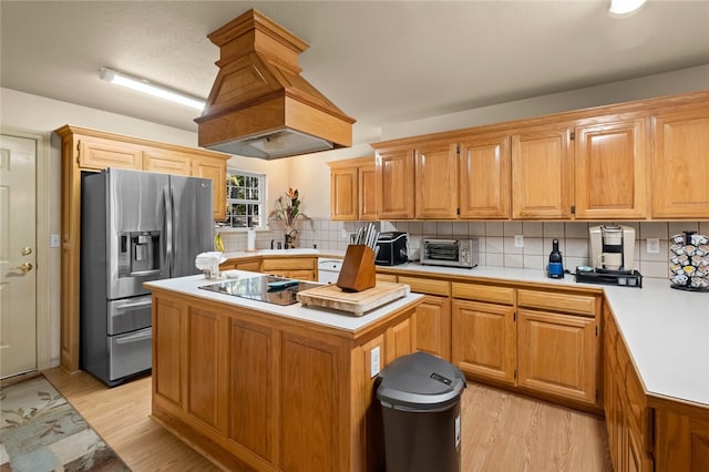 kitchen with decorative backsplash, stainless steel refrigerator with ice dispenser, custom range hood, light hardwood / wood-style flooring, and a kitchen island