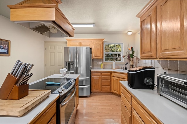 kitchen with sink, stainless steel appliances, tasteful backsplash, premium range hood, and light hardwood / wood-style floors