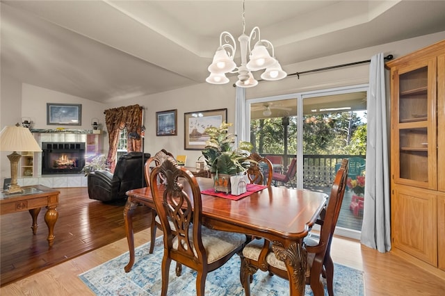 dining area featuring a raised ceiling, a tile fireplace, a notable chandelier, and light wood-type flooring