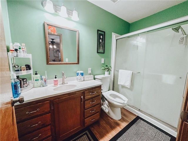 bathroom featuring toilet, a shower with shower door, hardwood / wood-style floors, ceiling fan, and vanity