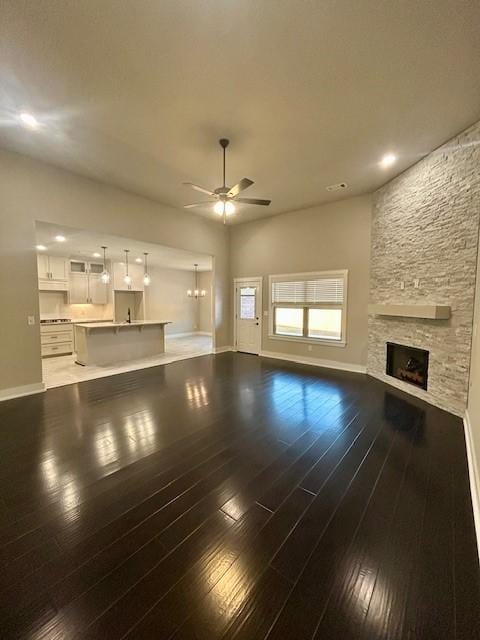 unfurnished living room with ceiling fan, a stone fireplace, and dark hardwood / wood-style floors