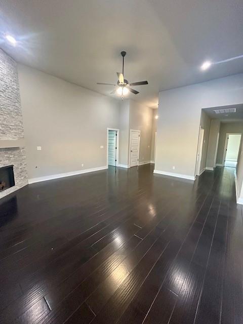 unfurnished living room with dark hardwood / wood-style floors, ceiling fan, and a stone fireplace