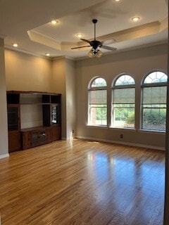 unfurnished living room featuring ceiling fan, a raised ceiling, hardwood / wood-style floors, and crown molding