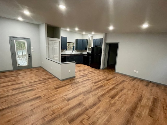 kitchen with light wood-type flooring, plenty of natural light, kitchen peninsula, and black refrigerator