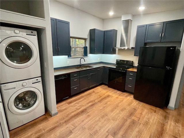 kitchen with wall chimney range hood, black appliances, sink, stacked washer and dryer, and light wood-type flooring