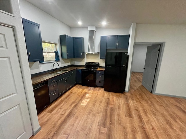 kitchen with wall chimney range hood, light hardwood / wood-style floors, black appliances, sink, and blue cabinets