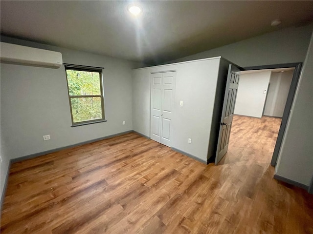 unfurnished bedroom with lofted ceiling, an AC wall unit, a closet, and hardwood / wood-style flooring