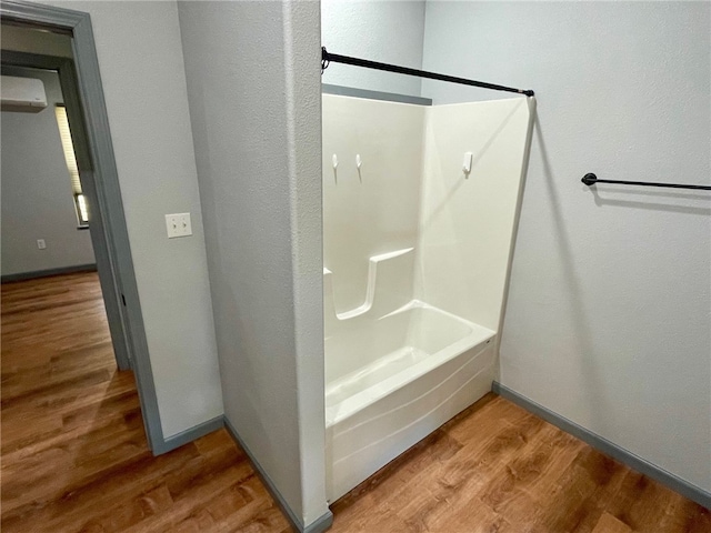 bathroom featuring wood-type flooring, bathing tub / shower combination, and a wall unit AC