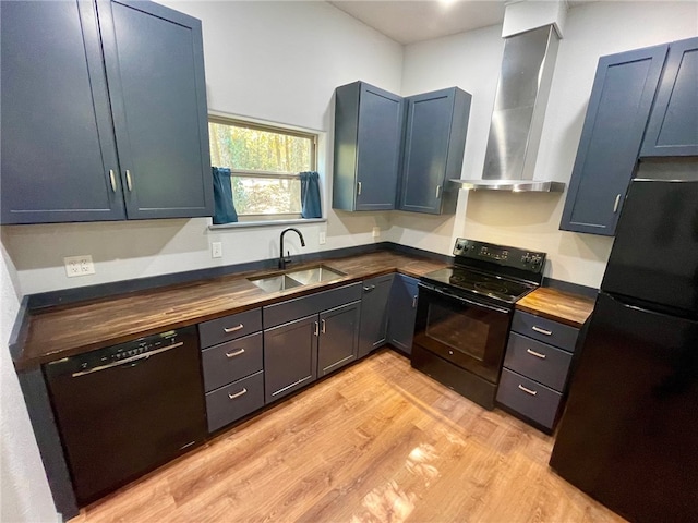 kitchen with butcher block counters, blue cabinetry, wall chimney range hood, black appliances, and sink