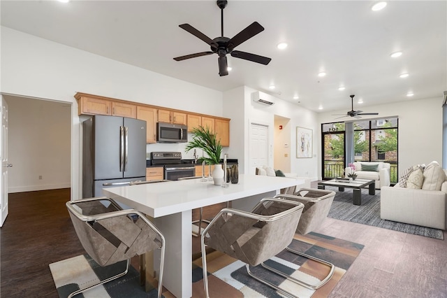 kitchen with dark wood-type flooring, an island with sink, a kitchen bar, appliances with stainless steel finishes, and ceiling fan